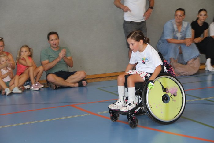 Eine der Teilnehmerinnen des Rollstuhl-Slaloms absolviert den Parcours. Im Hintergrund sieht man die Zuschauer, die sie anfeuern. 